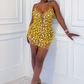 Woman in a yellow sequin dress posing against a white wall.