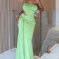 Woman in a green evening gown standing indoors with a neutral background